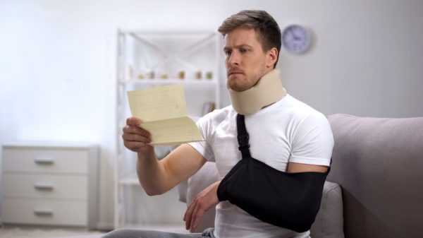 Man in foam neck brace and arm sling reading medical bill, shocking price