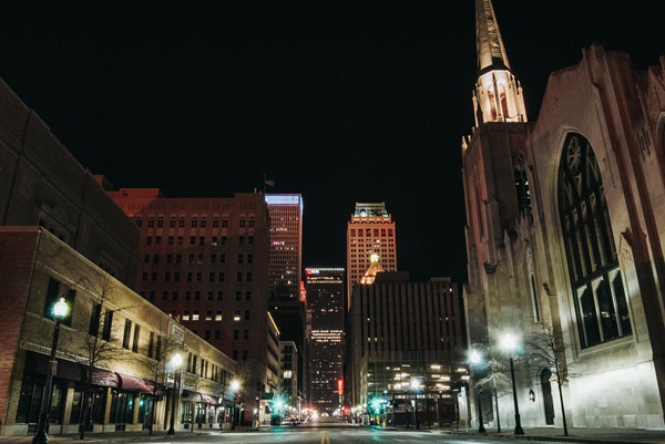 Downtown Tulsa, Oklahoma street at night with illuminated buildings, traffic lights, and a church with a tall steeple on the right.
